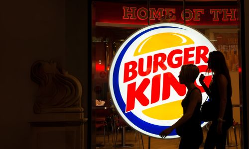 Two people walking walking in front of the Burger King lit up sign 