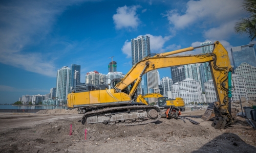 Yellow bulldozer working on a development site in Miami with Miami skyline in the back.
