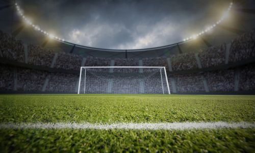Soccer goal centered on a stadium field under bright lights with a packed crowd in the background.