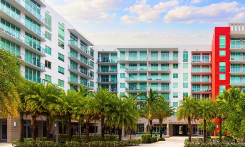 Building with apartments in the commercial area of miami neighborhood, with red and gray colors you can see balconies, shops, tropical climate, palm trees and flower beds