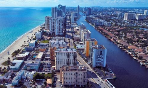 Aerial view of beachfront and intracoastal condominium buildings in South Florida, highlighting dense coastal development and mixed-use structures.