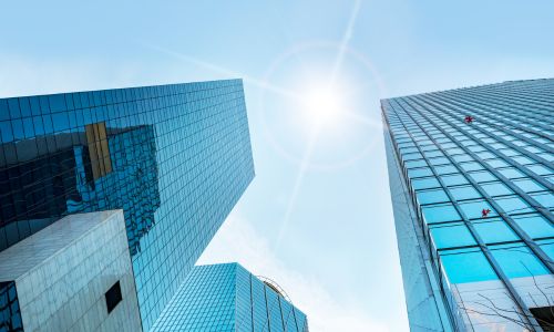 Image of corporate buildings taken at an upward angle with the sun in the sky