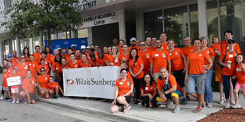 Group of Bilzin Sumberg employees holding a Bilzin Sumberg sign at a recent Bilzin Sumberg Cares Day event. 